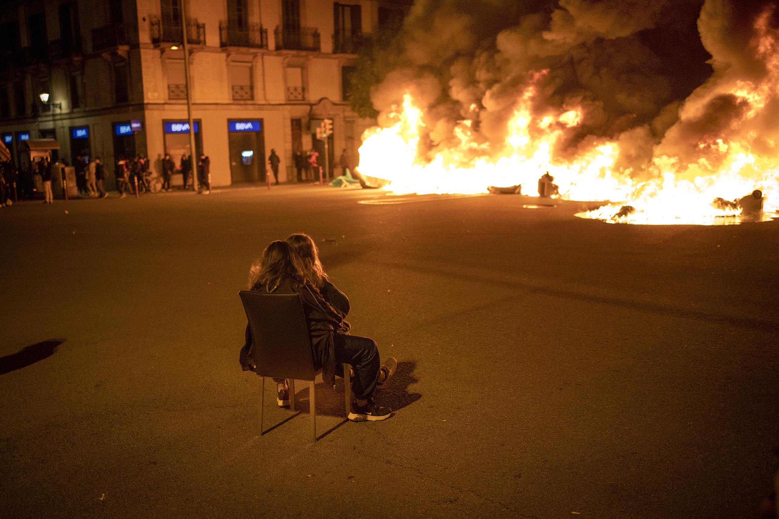 Dos mujeres sentadas contemplan una barricada en llamas erigida por manifestantes durante una protesta contra el arresto del rapero Pablo Hasél, en Barcelona, España.
