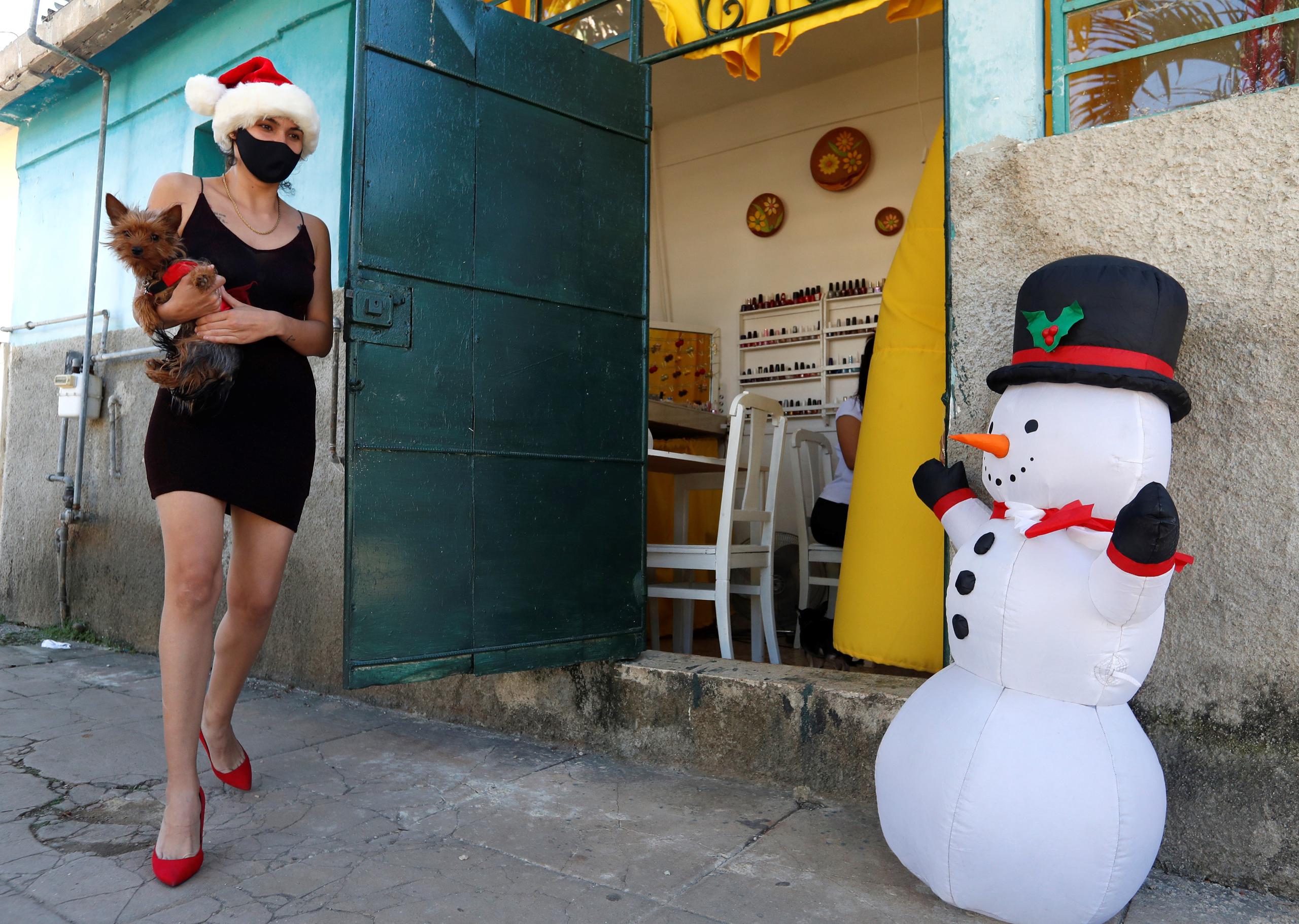 Una mujer con gorro navideño pasa caminando frente a un muñeco de nieve inflable, en La Habana, en una fotografía de archivo. EFE/Yander Zamora
